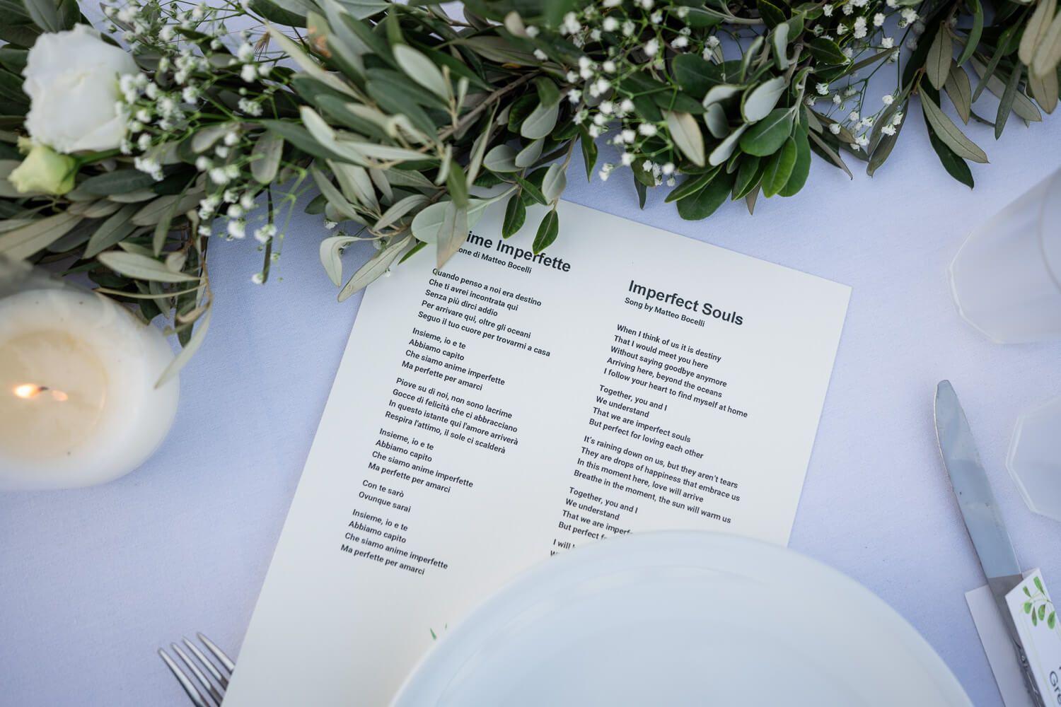 Wedding program menu card displayed on table with white flowers and a glowing candle decoration.