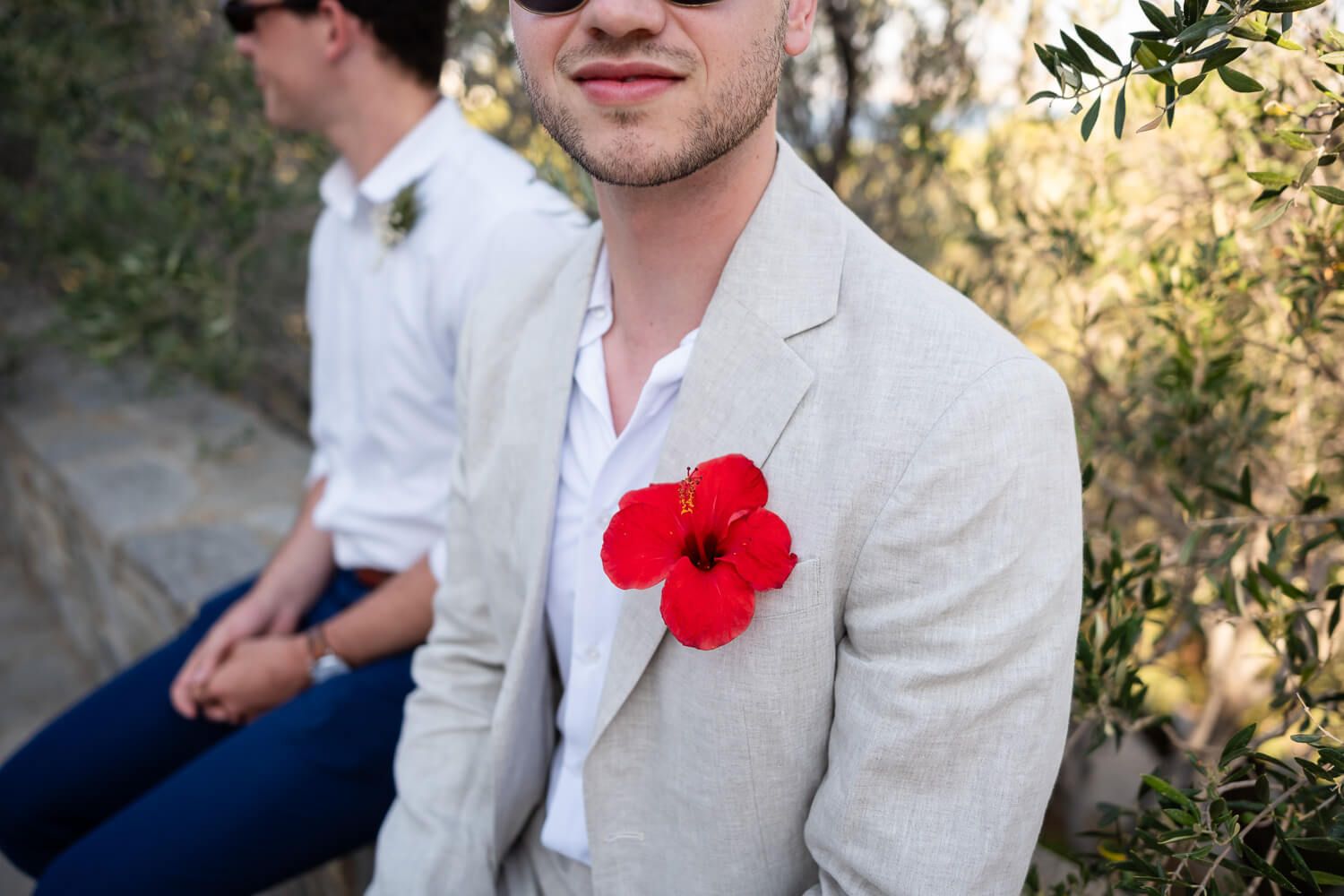 Guest wearing white suit with red flower boutonniere during a wedding celebration in Paros.