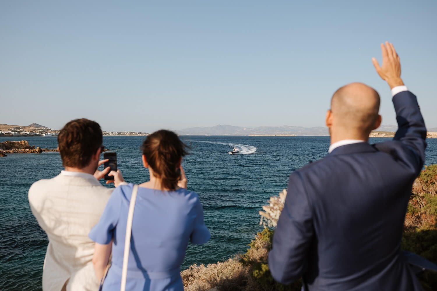 Groom waiving at his bride outside a traditional Cycladic chapel