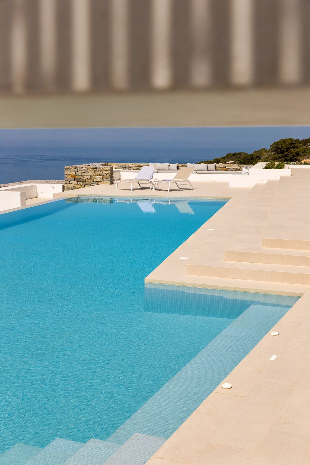 Luxury pool with crystal blue water and stone terrace overlooking the sea at a Greek island villa.