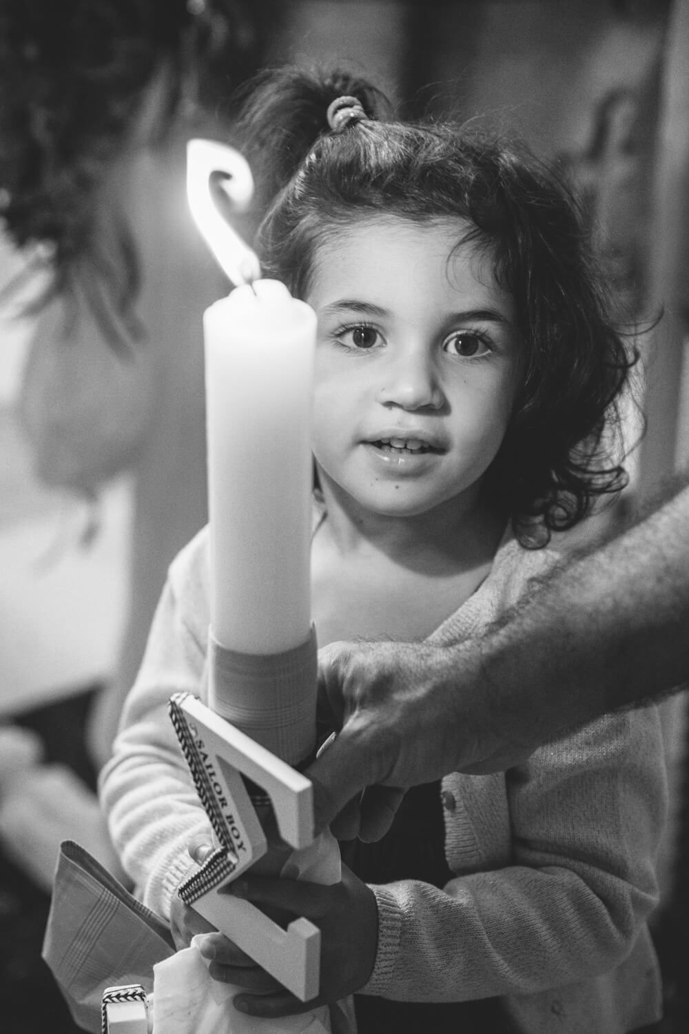Young girl holding a large white candle and a cross in a black and white religious ceremony photo.