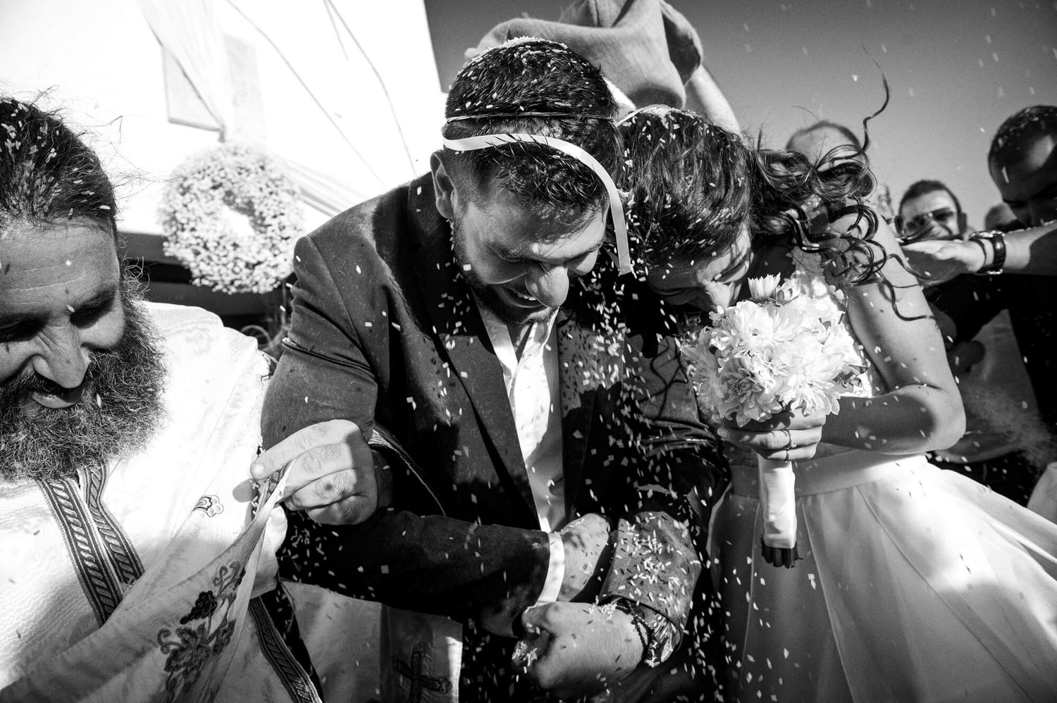 Black and white photo of bride and groom being showered with rice during a joyful outdoor wedding ceremony in Paros Greece.