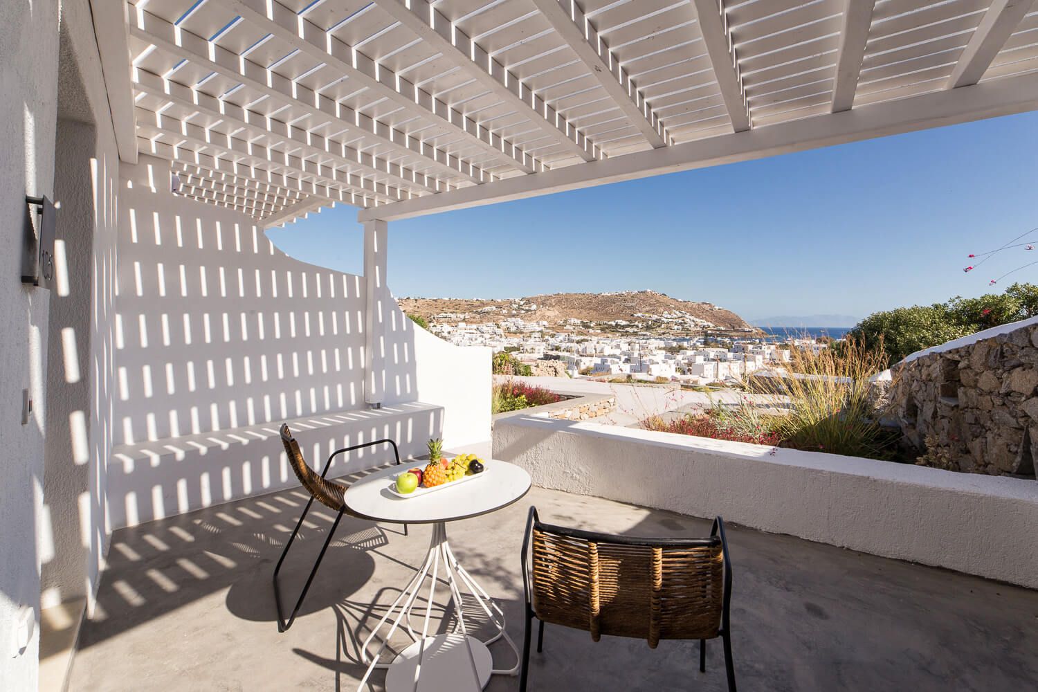 Scenic Mediterranean terrace with white pergola and bistro set overlooking coastal town and hillside views.