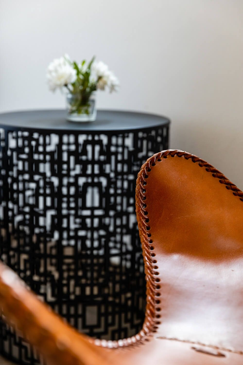 Close-up of a brown leather chair with stitching, beside a black side table with white flowers.