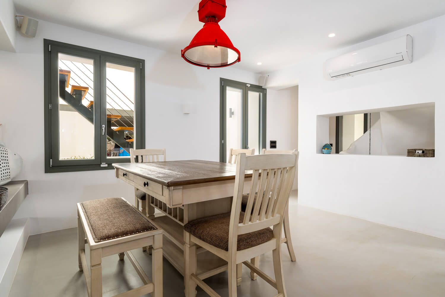 Modern white dining room features wooden table and chairs with red pendant light in a luxury villa in Paros
