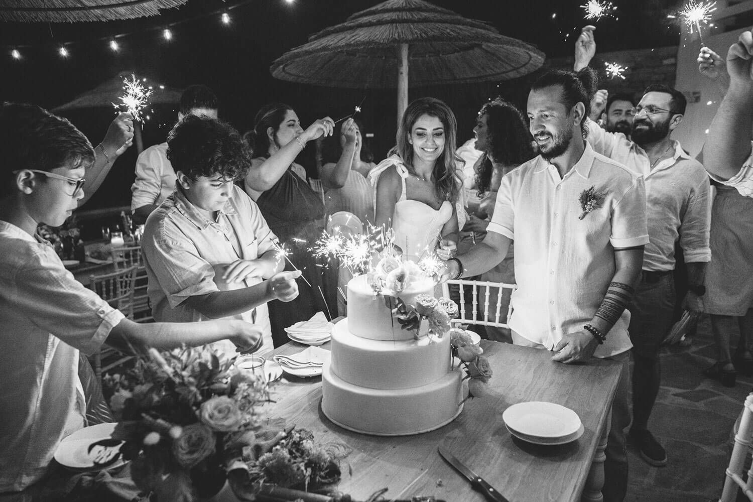 A black and white image of a wedding celebration showing sparklers, cake cutting and joyful moments at the reception.