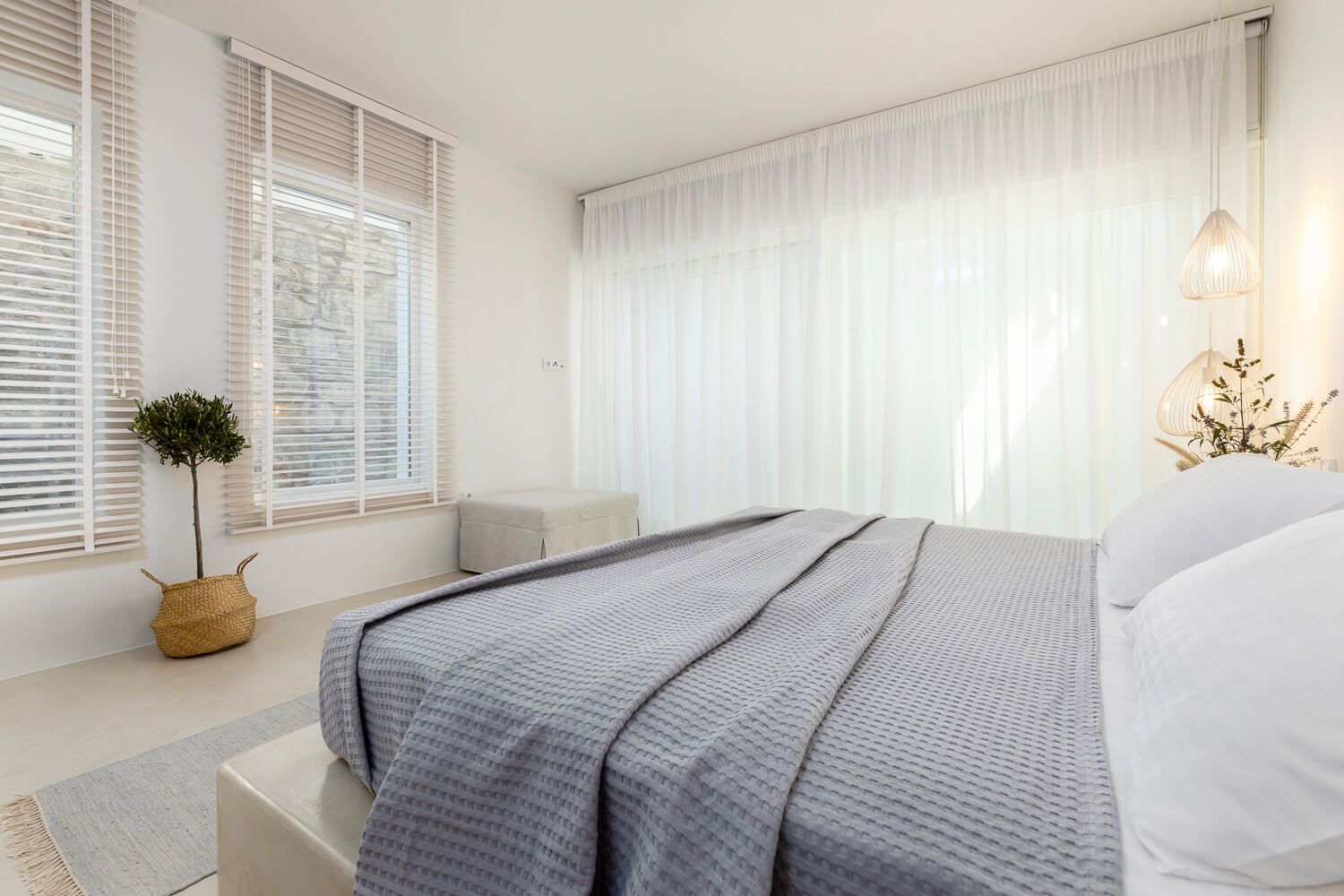 Modern white bedroom interior with grey bedding, natural light, and minimalist decor showcases a clean Scandinavian design.