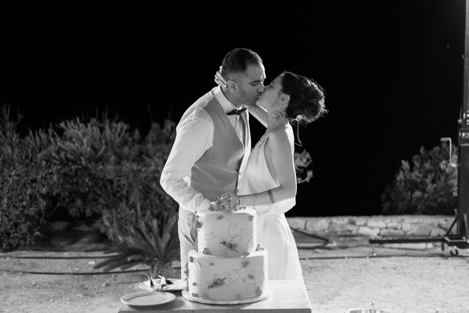 Couple kissing in front of their wedding cake during the reception at villa Komito
