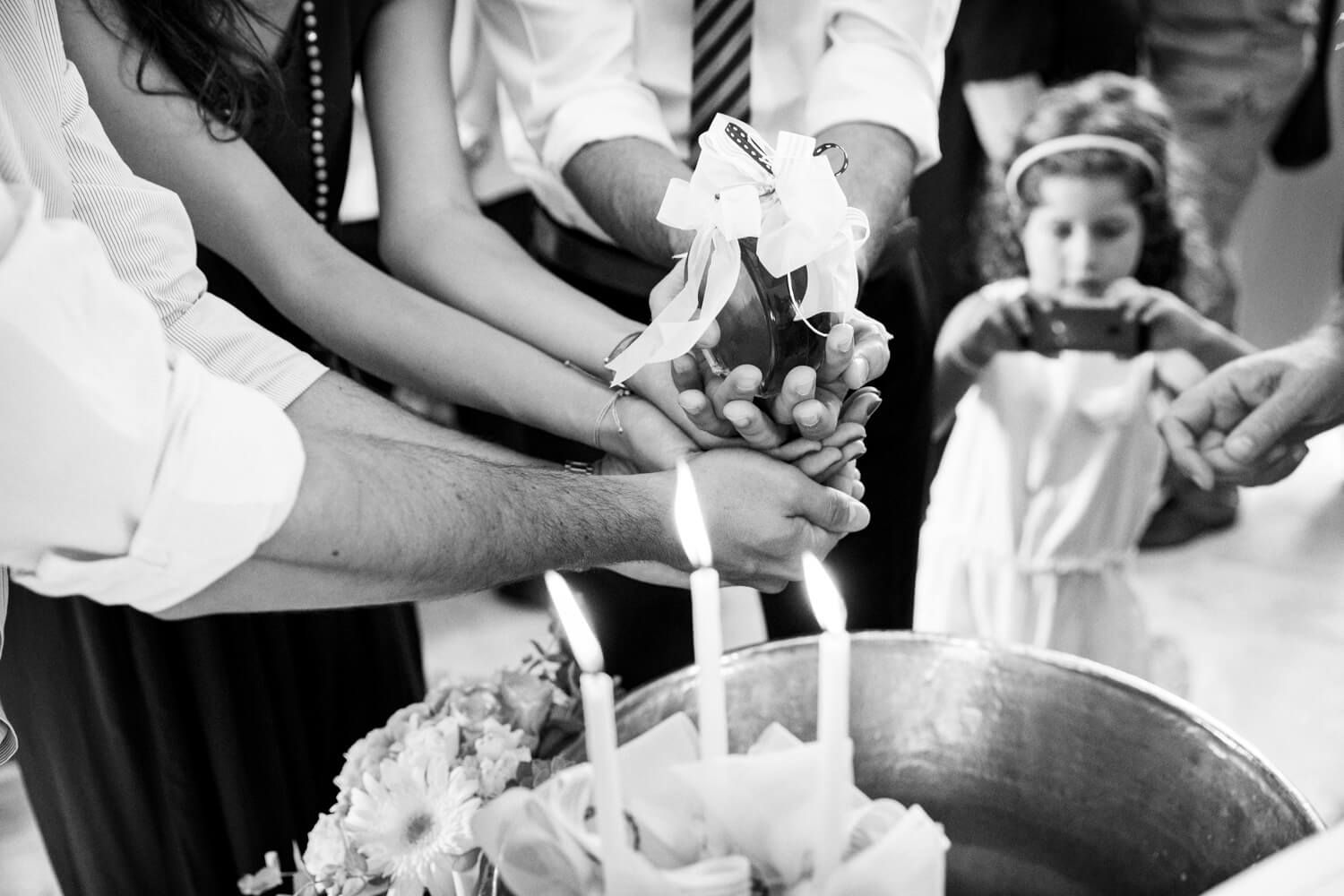 Close-up black and white photo of hands holding oil over a baptismal font during a christening.