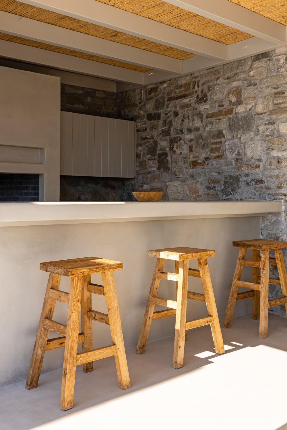 Rustic wooden bar stools line a white counter against a stone accent wall with exposed wooden ceiling beams.