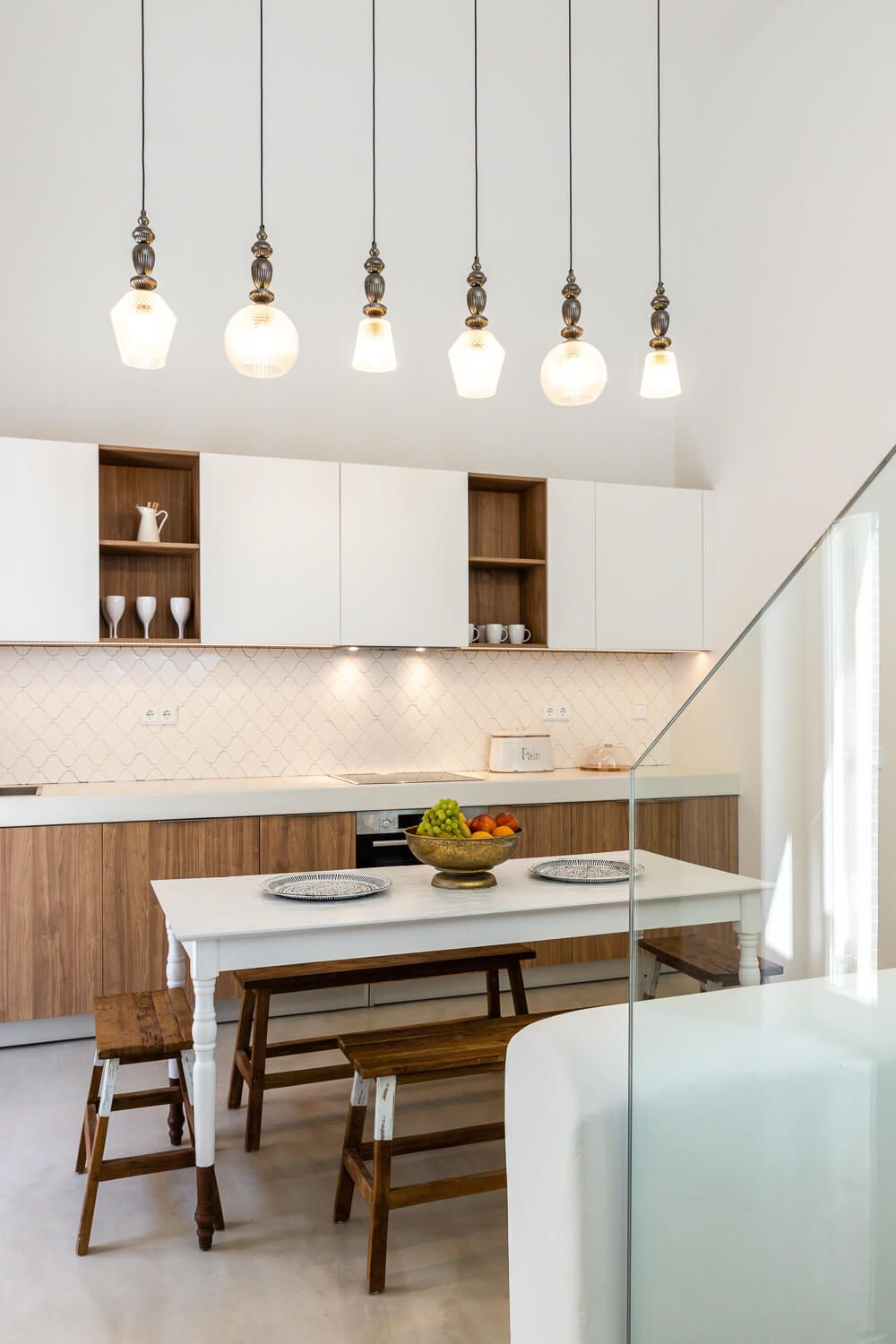 Modern kitchen with pendant lights, wood cabinets and a dining island with wooden benches.