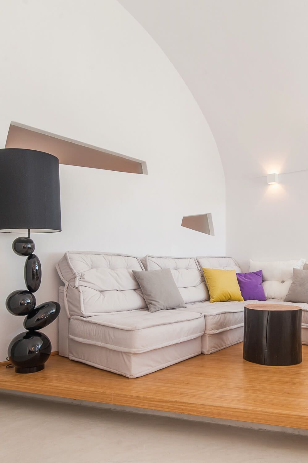 Modern living room with white sectional sofa on wooden platform featuring black lamps and colorful accent pillows.