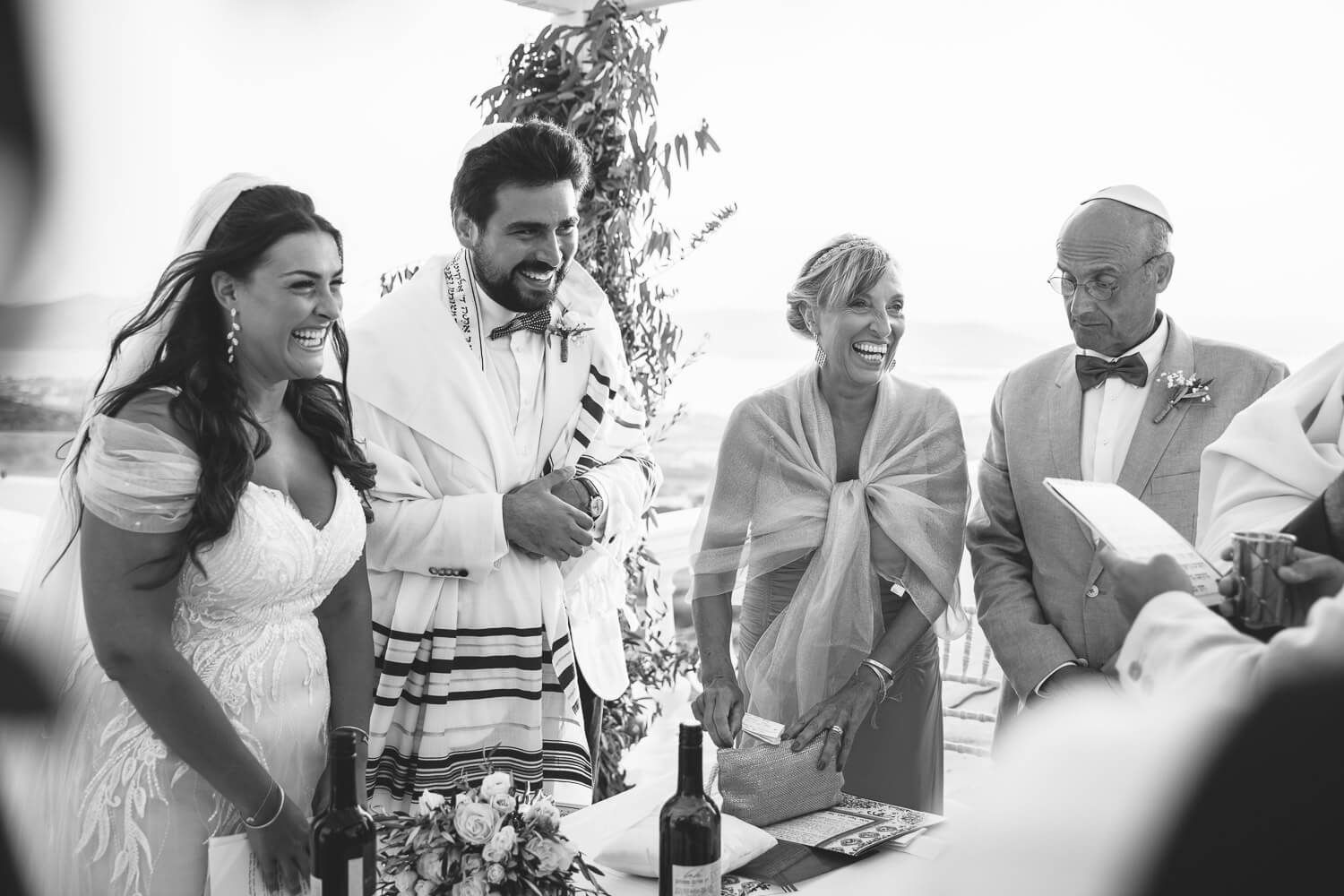 A b&w photo shows candid moments of people at a jewish wedding at Villa Aethra Paros Greece.