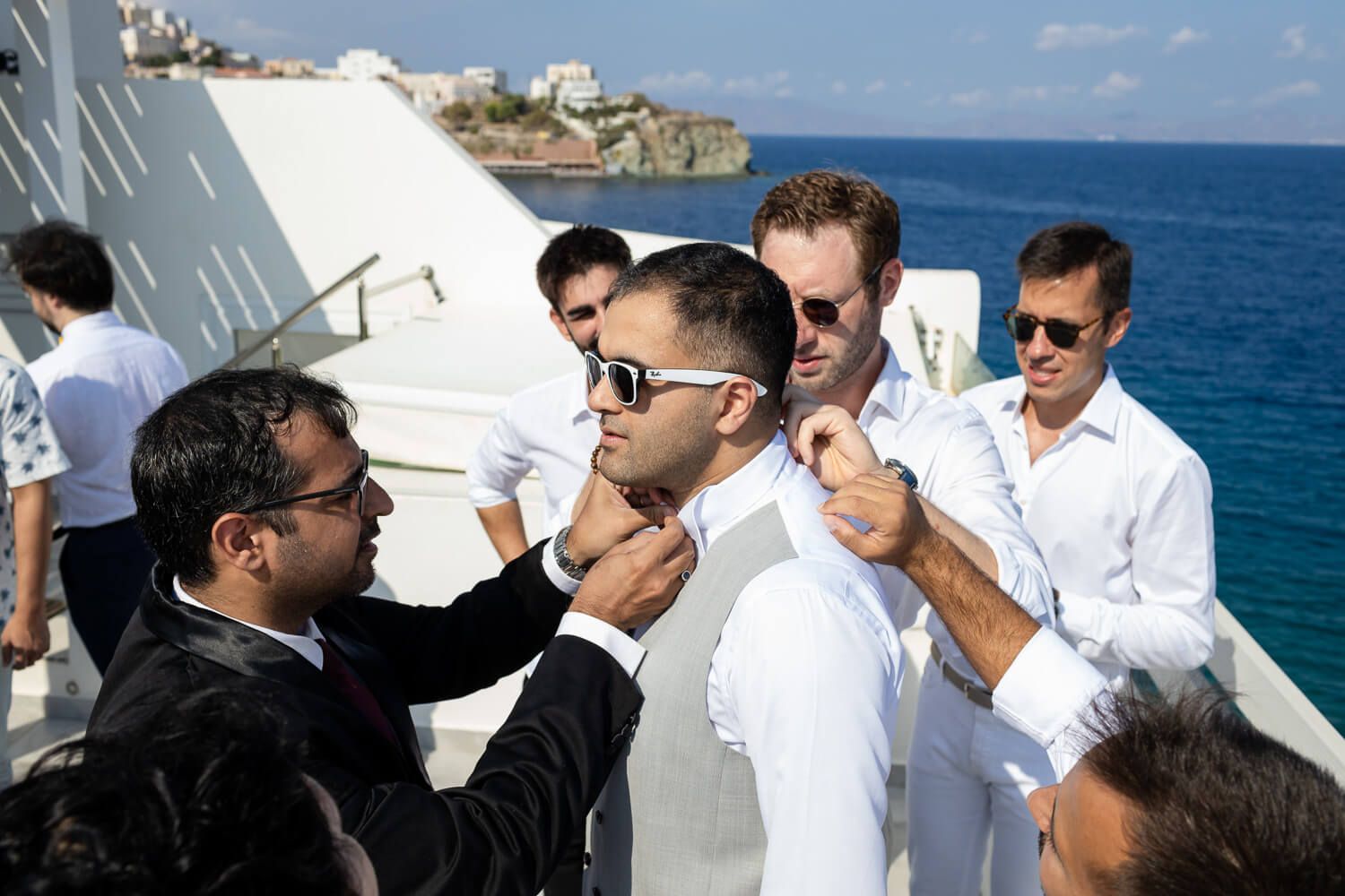 Groomsmen helping Akshay put on his suit jacket in Ermoupolis