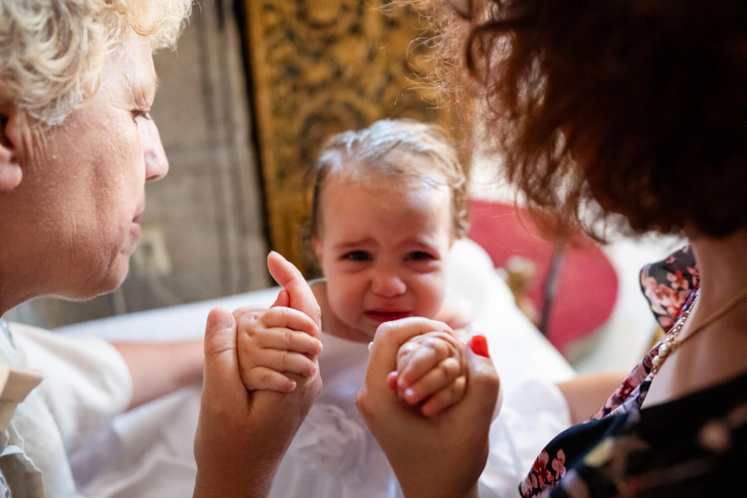 Grand parents holding a crying baby girl in a white dress during a baptism ceremony in Paros island.