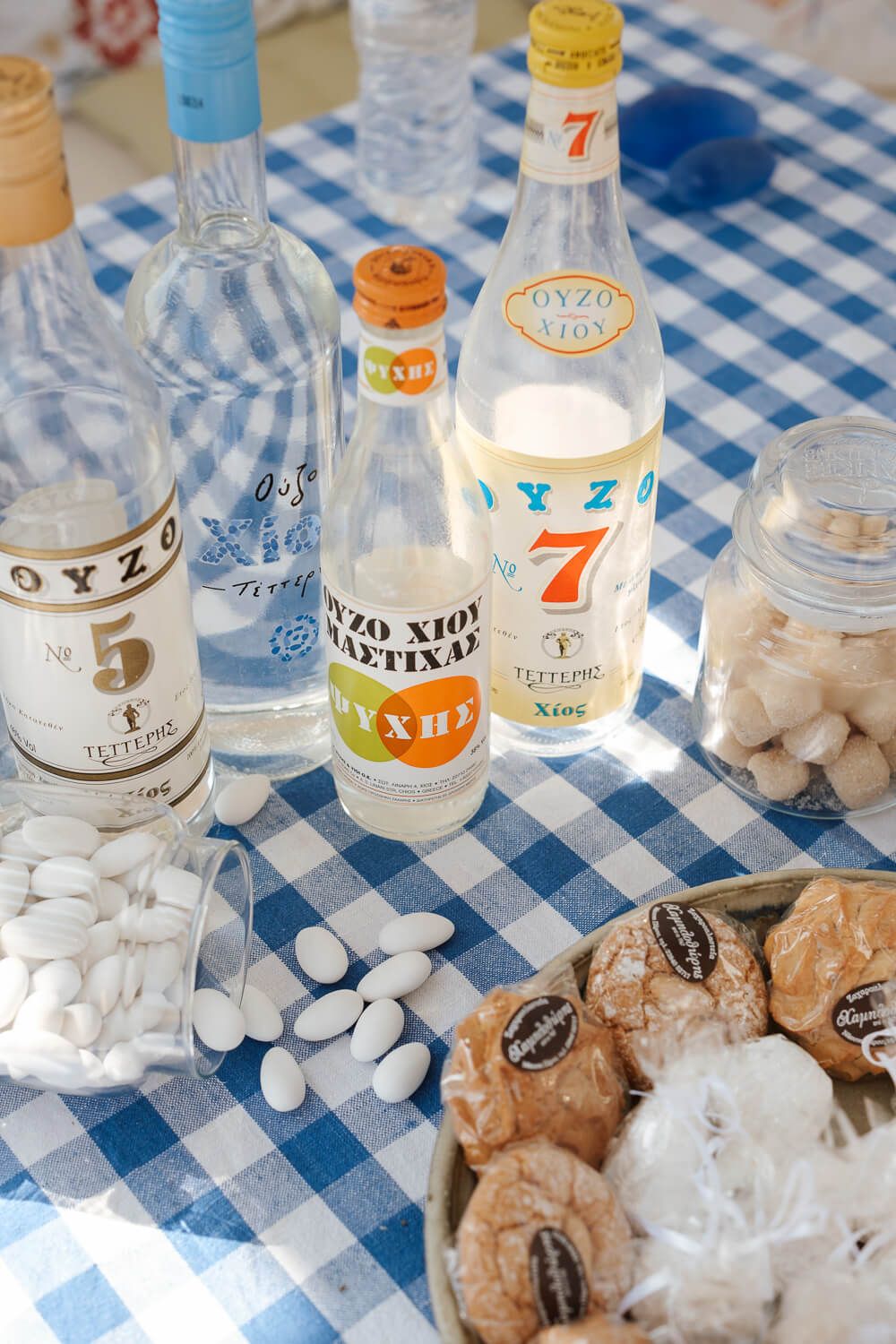 Traditional Greek ouzo bottles and sugared almonds on blue checkered tablecloth.