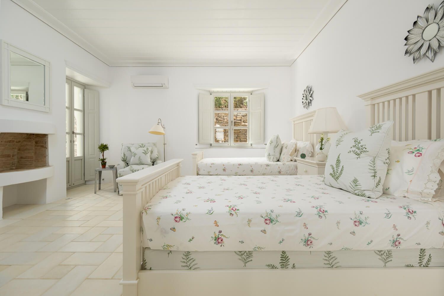 Bright coastal bedroom with twin beds featuring floral bedding, built-in window seat and white furnishings in beach house style.