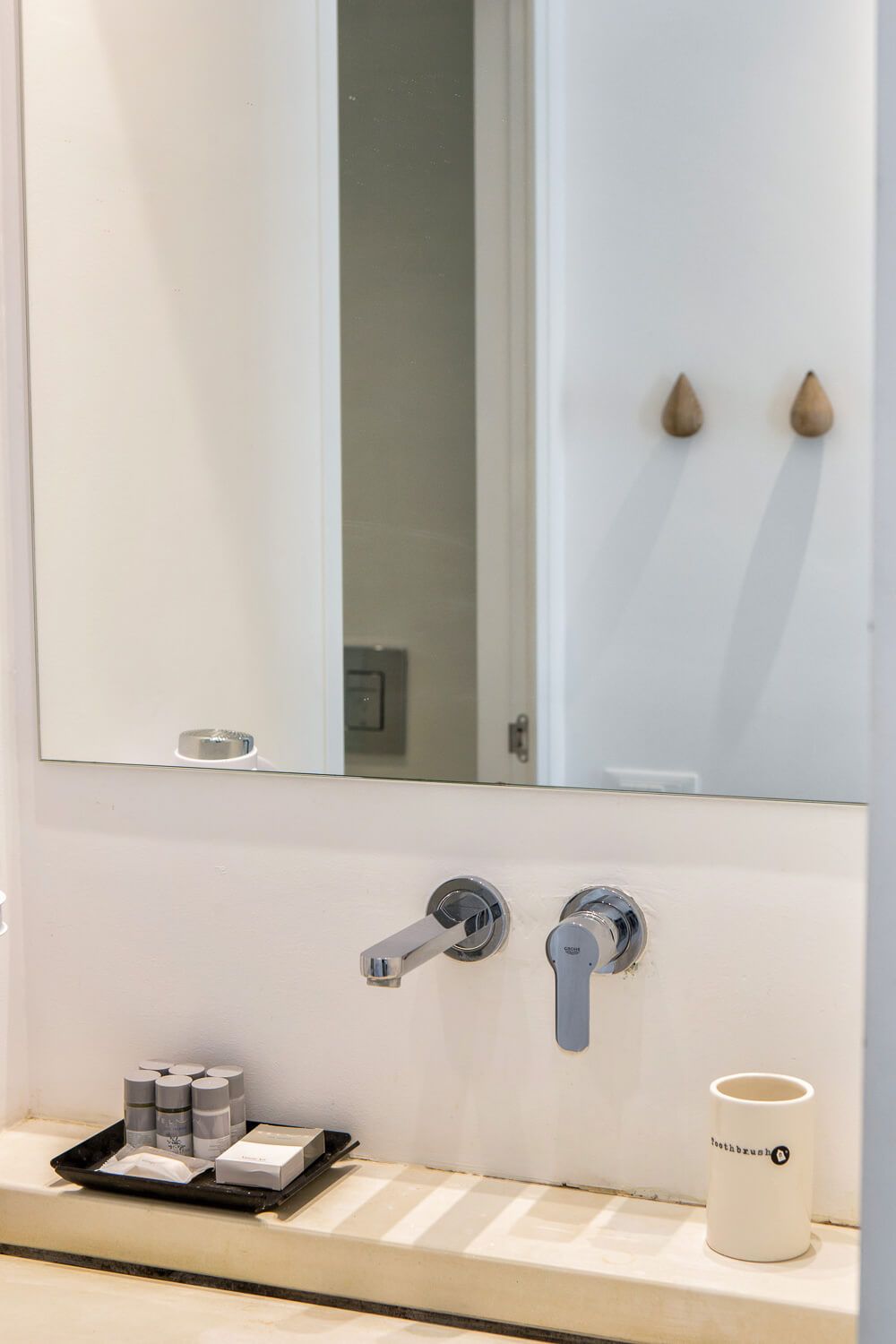 Modern minimalist bathroom interior with white walls, wooden countertop, and sleek faucet fixtures.