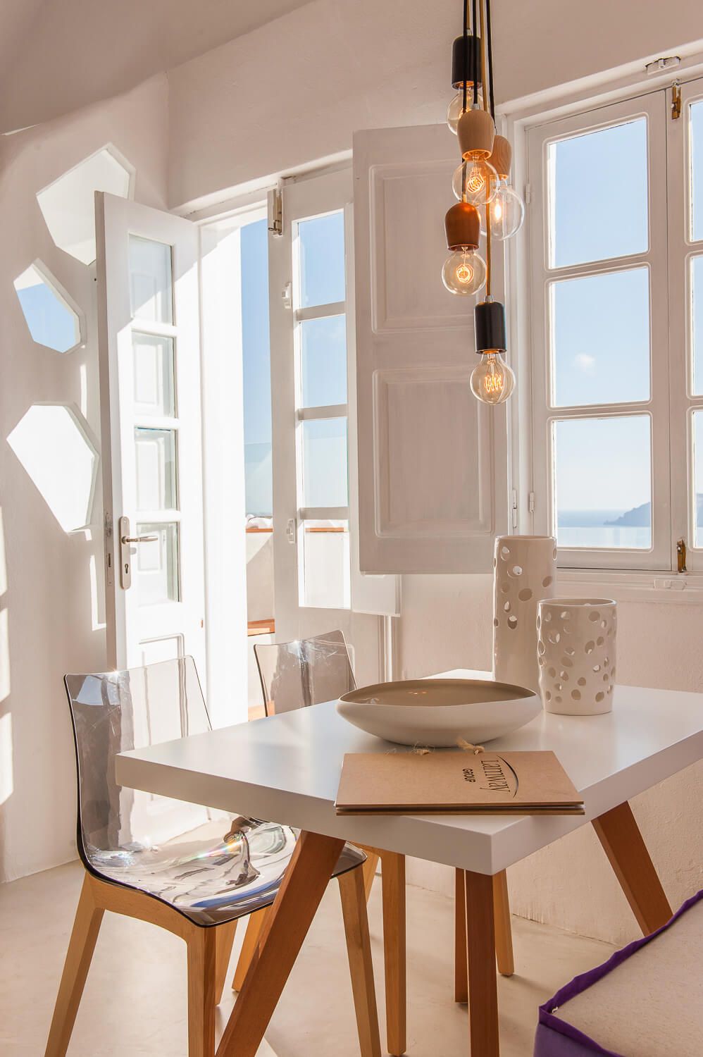 Bright white dining area with stunning sea view through open windows in Santorini.