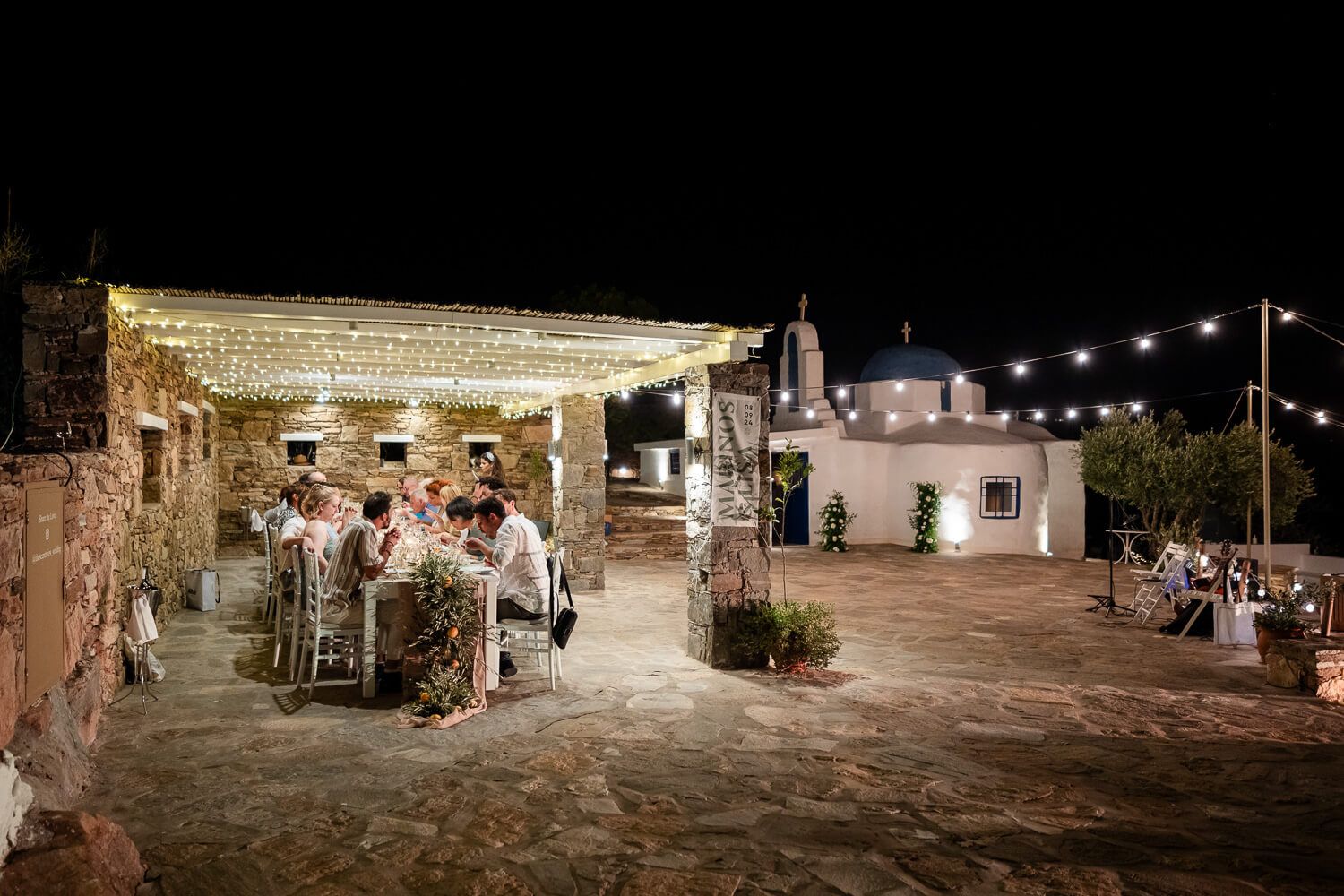 Guests taking their seats at the long wooden table under the fairy lights