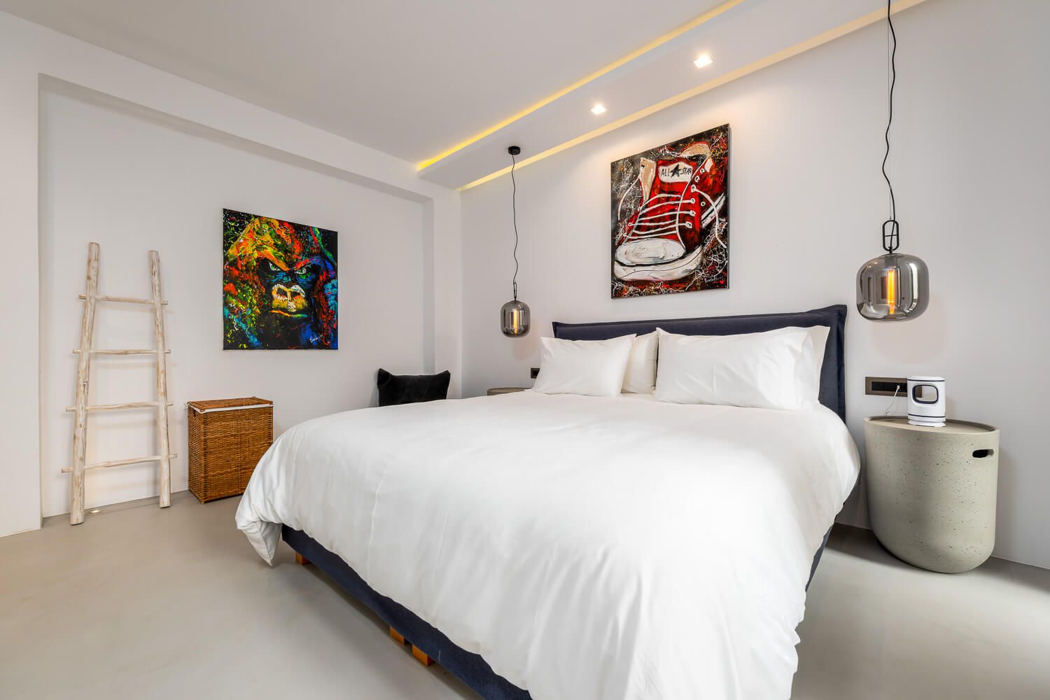 Modern hotel room with white bedding, colorful artwork, pendant lights, and warm accent lighting.