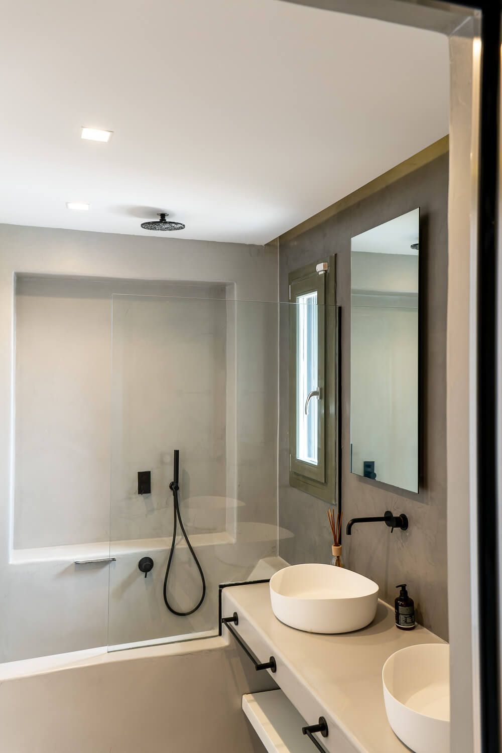 Modern minimalist bathroom with white vessel sinks, black fixtures, and a glass-enclosed shower area.