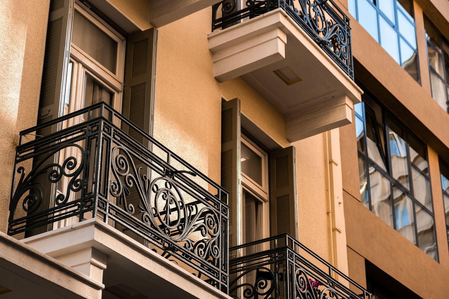 Ornate wrought iron balconies adorn a beige apartment building facade in a classic architectural style in Athens captured by Michael Salis