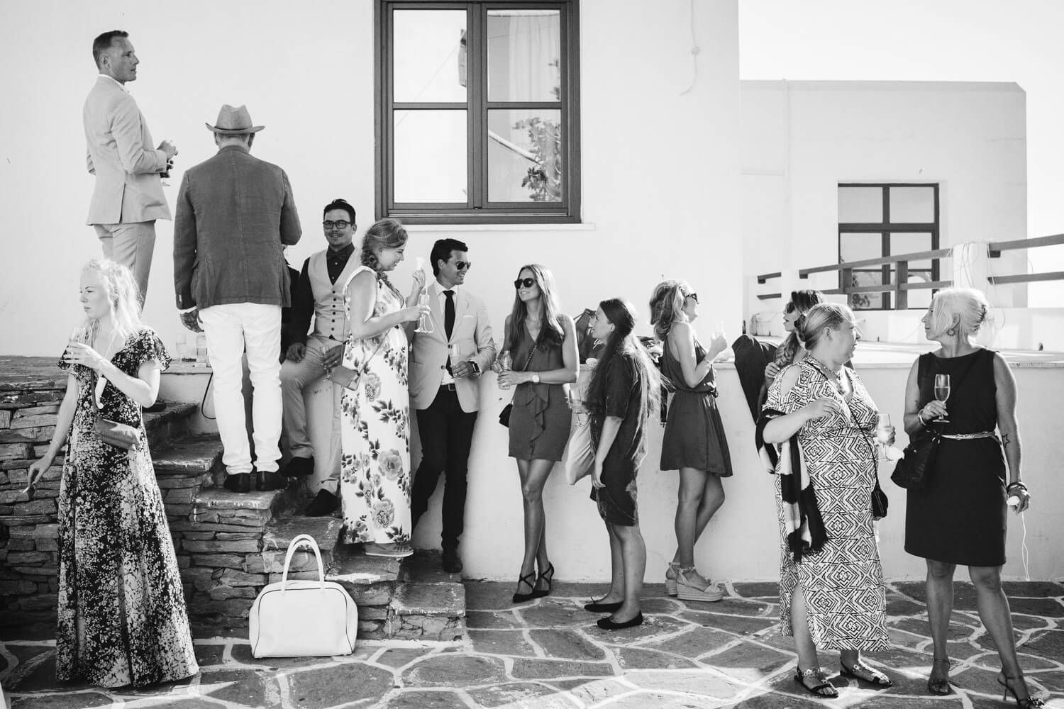 Black and white photo of guests socializing outside Paros Townhall at a summer wedding event.