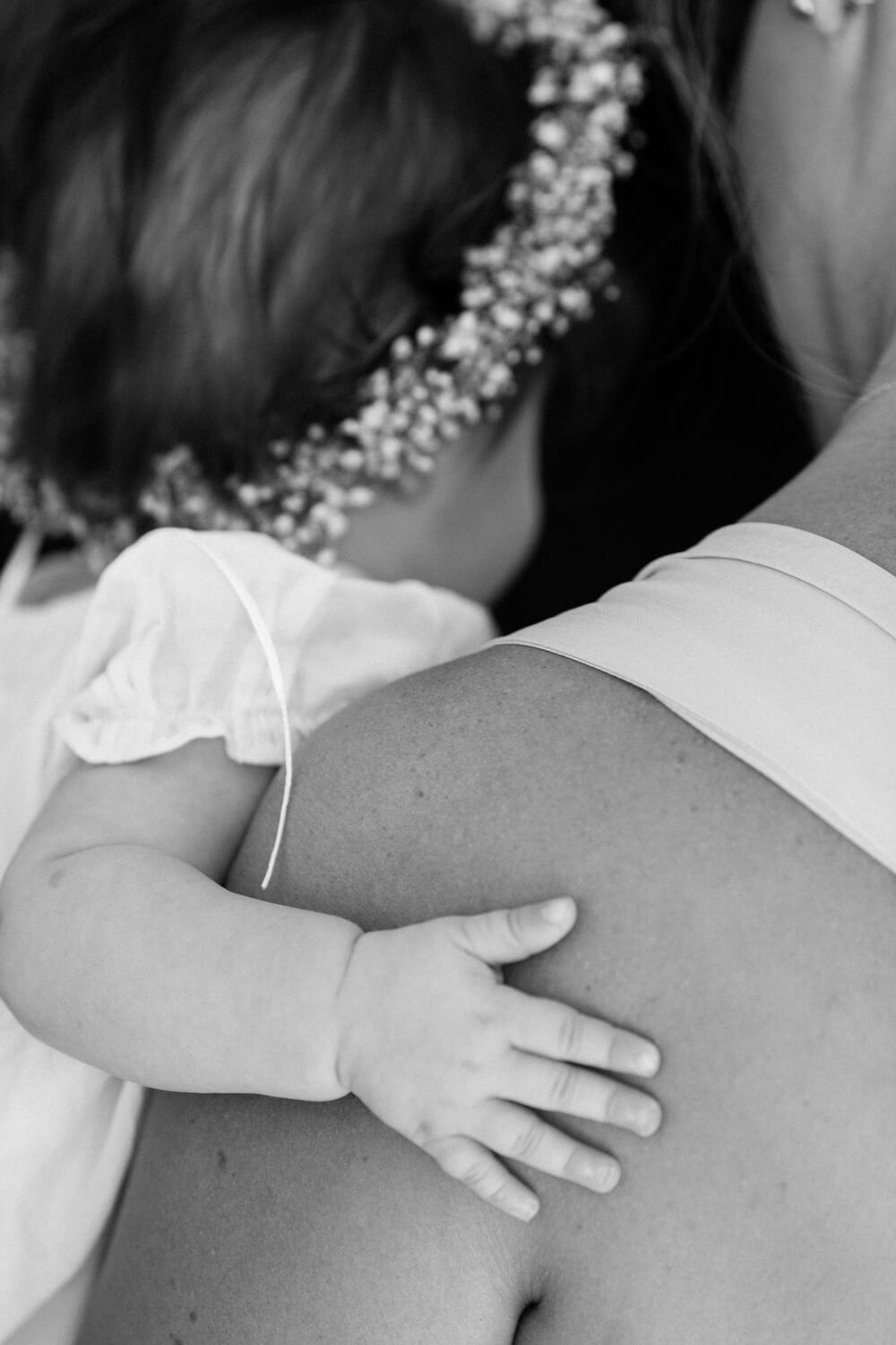 Black and white photo of a baby resting hand on mothers shoulder wearing floral crown.