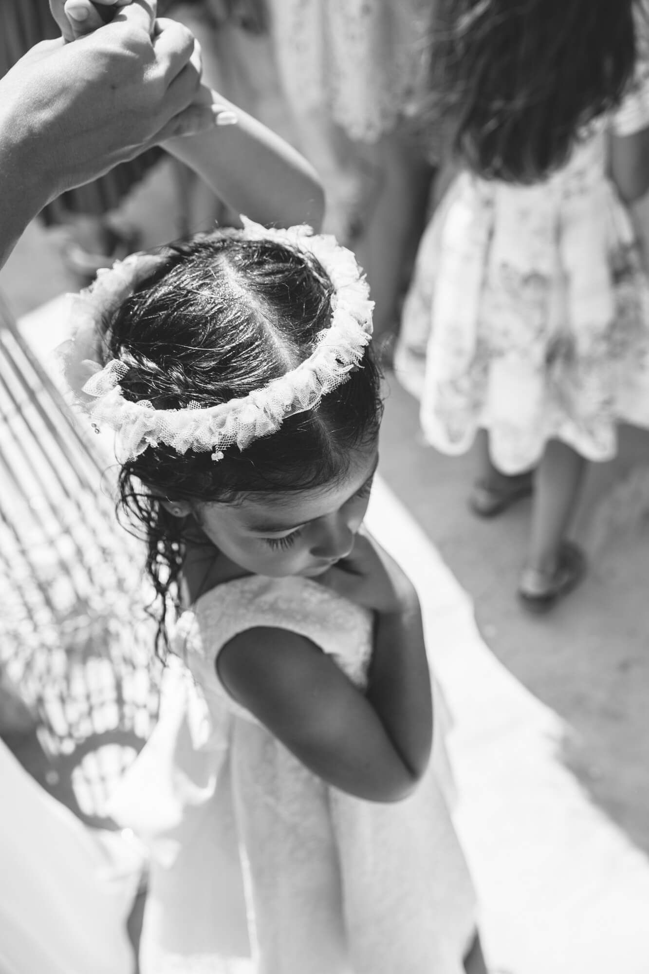 Black and white photo of a young flower girl wearing a floral crown at a baptism ceremony.