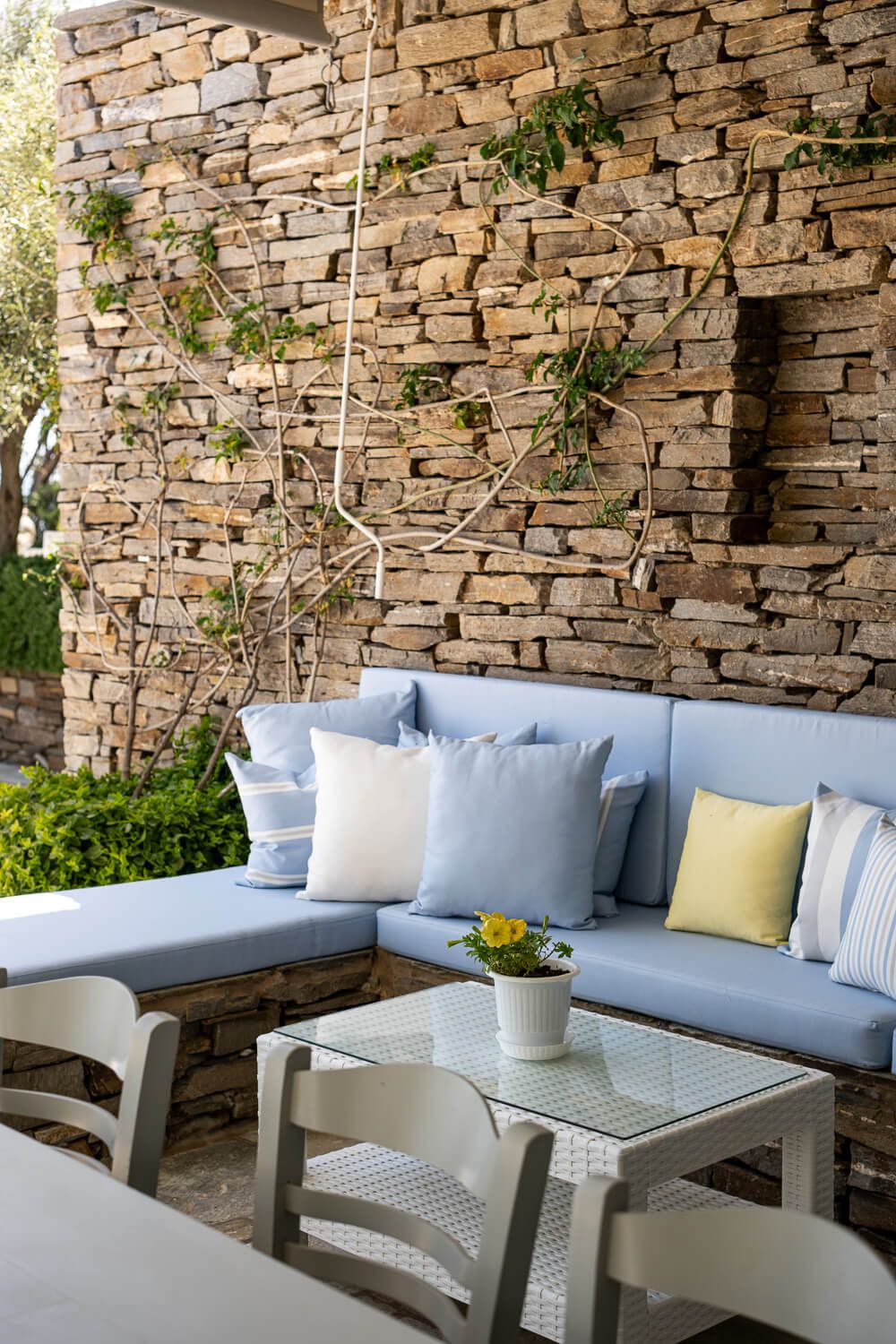 Modern outdoor patio furniture with light blue cushions against a natural stone wall creates an inviting seating area.