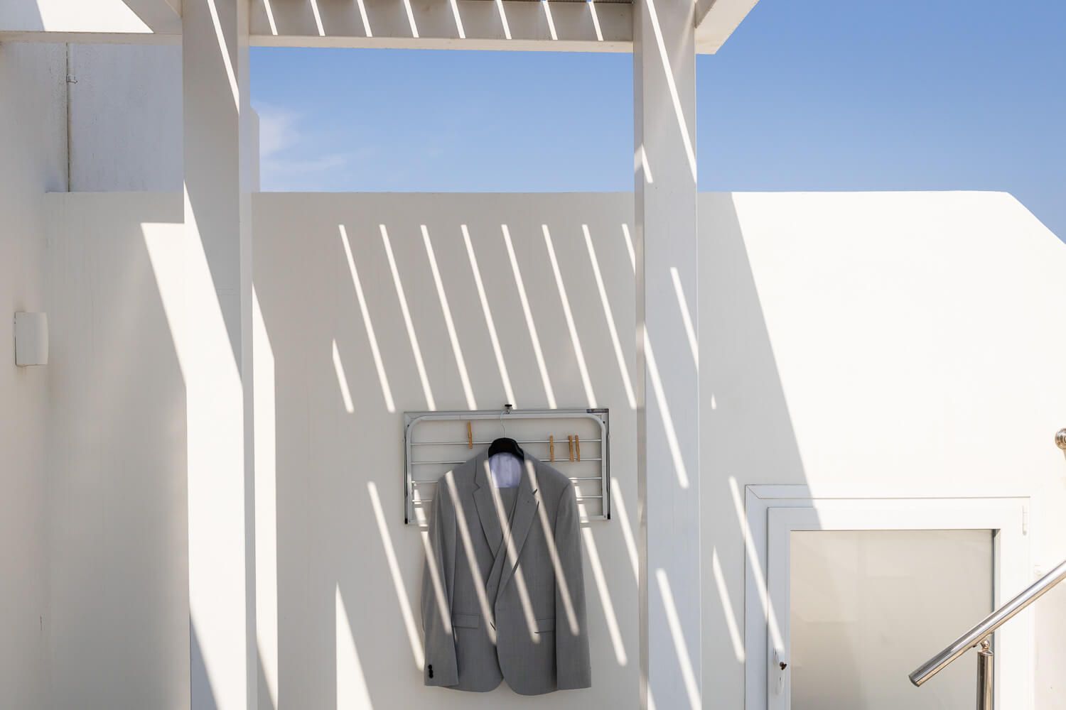 Shot of groom's suit agains a white wall in Ermoupolis Greece
