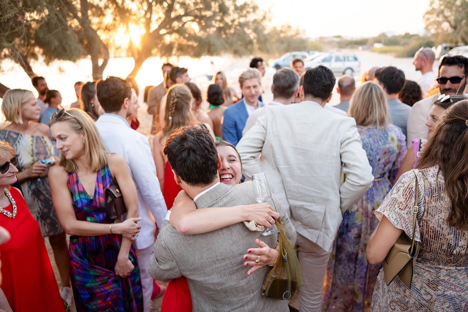 A large group of people hugging the groom at an outdoor sunset wedding reception celebration.