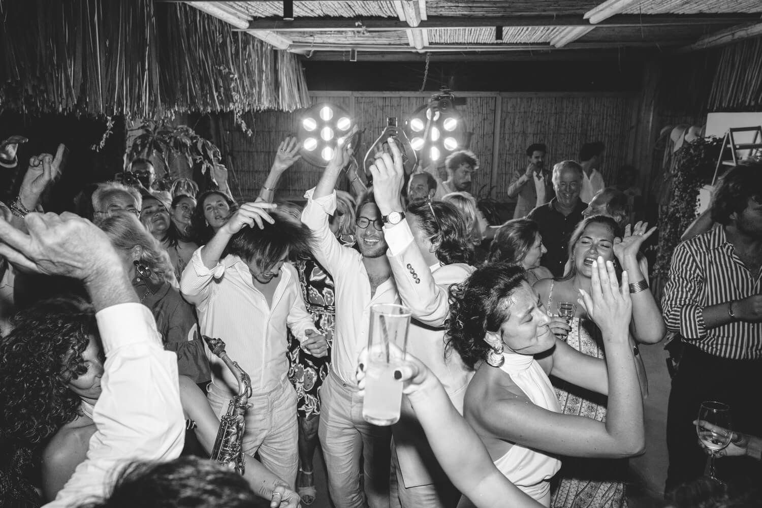 Lively black and white wedding dance floor packed with celebrating guests under bright lights.