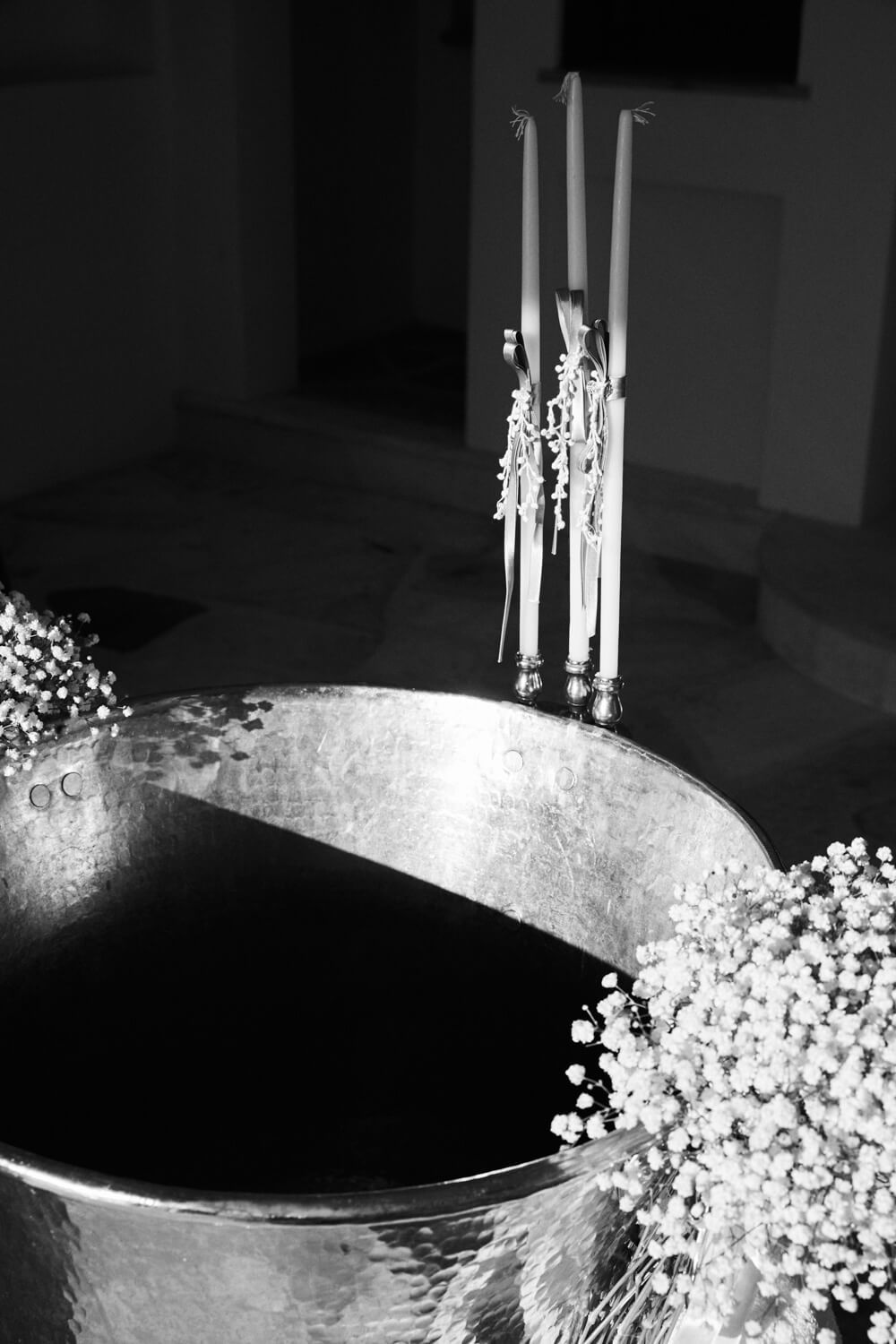 Black and white photo of baptism font with candles and baby's breath flowers.
