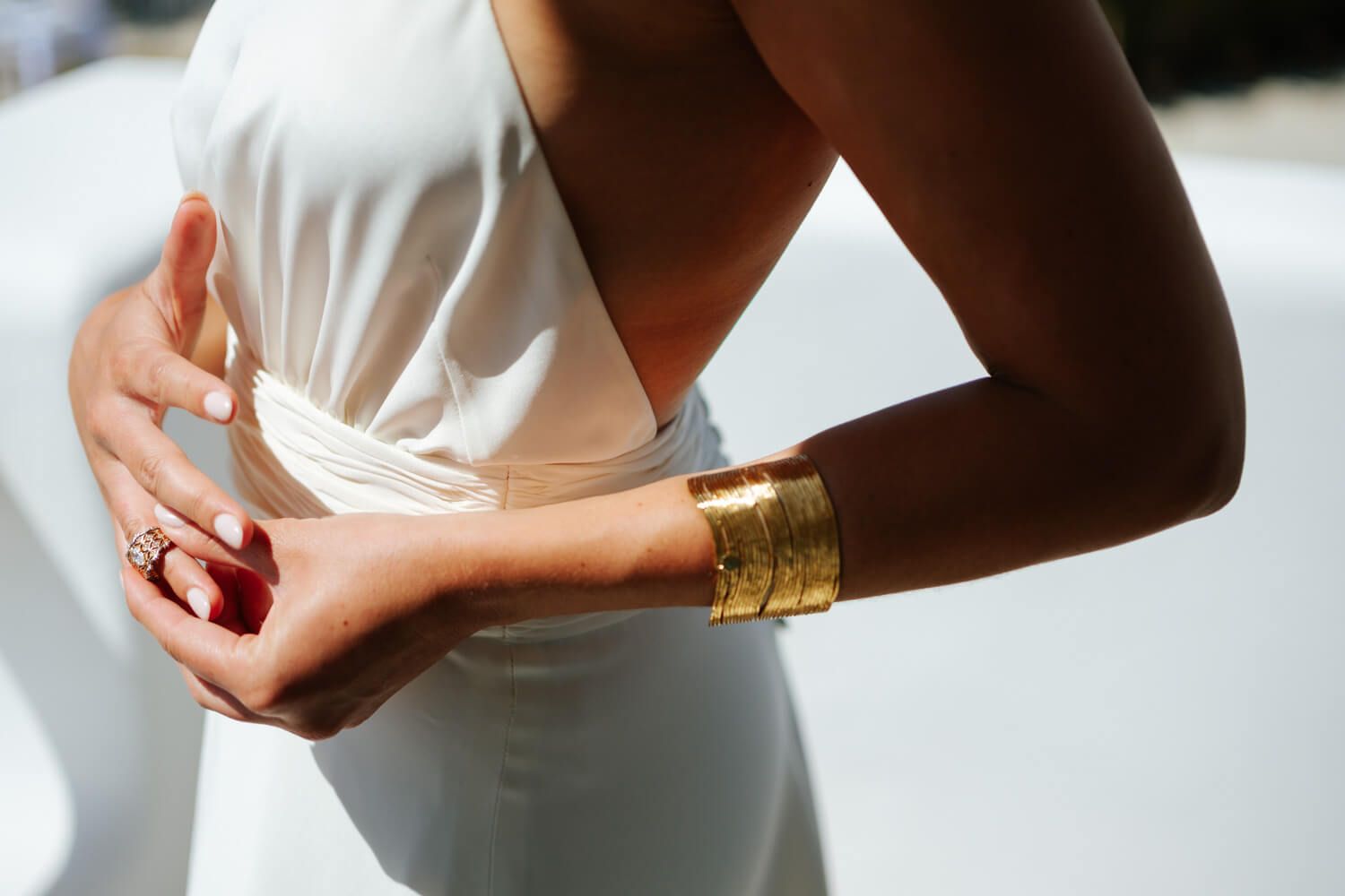 Woman in white dress wearing a gold cuff bracelet and ring, elegant bridal fashion accessories.