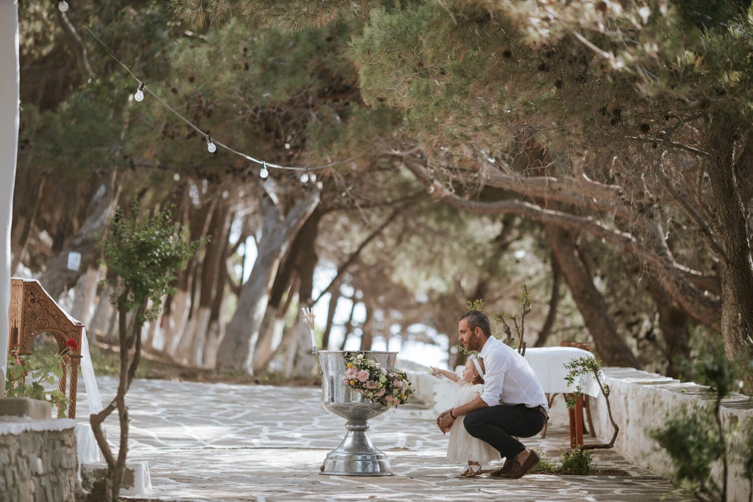 Father and child beside elegant floral arrangement  at outdoor christening venue.