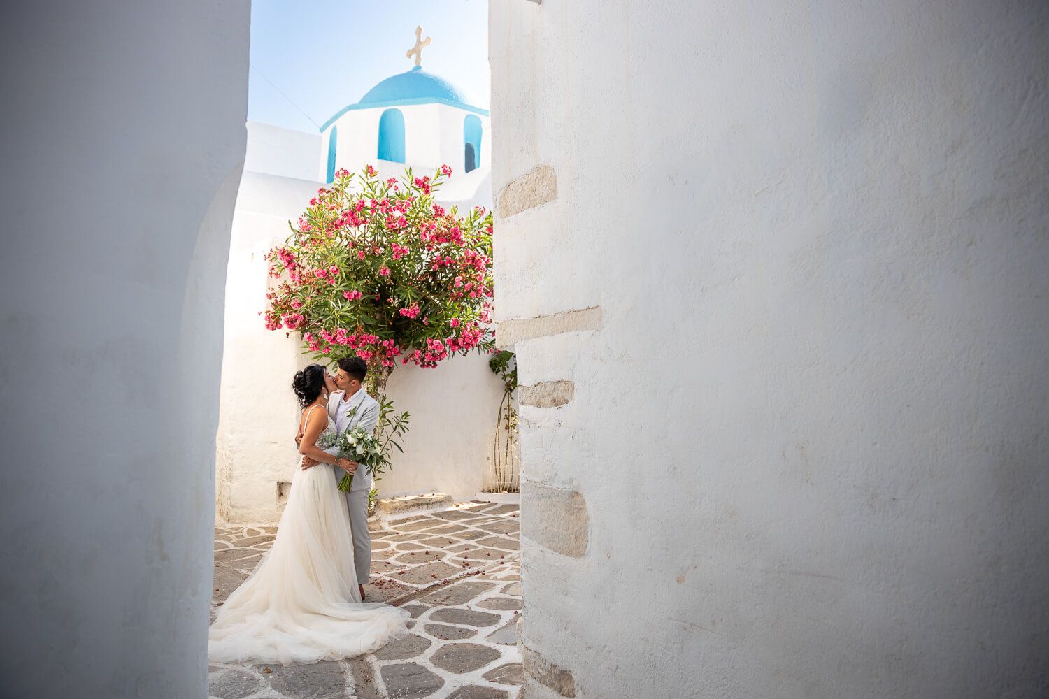 Groom kissing the bride's forehead under a blooming bougainvillea