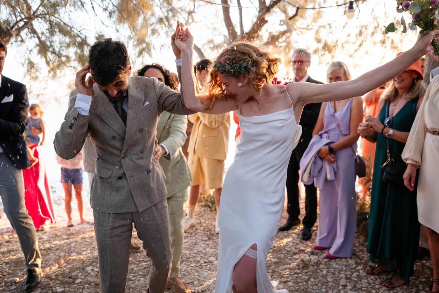 Bride and groom dancing joyfully outdoors at wedding reception with guests watching in background.