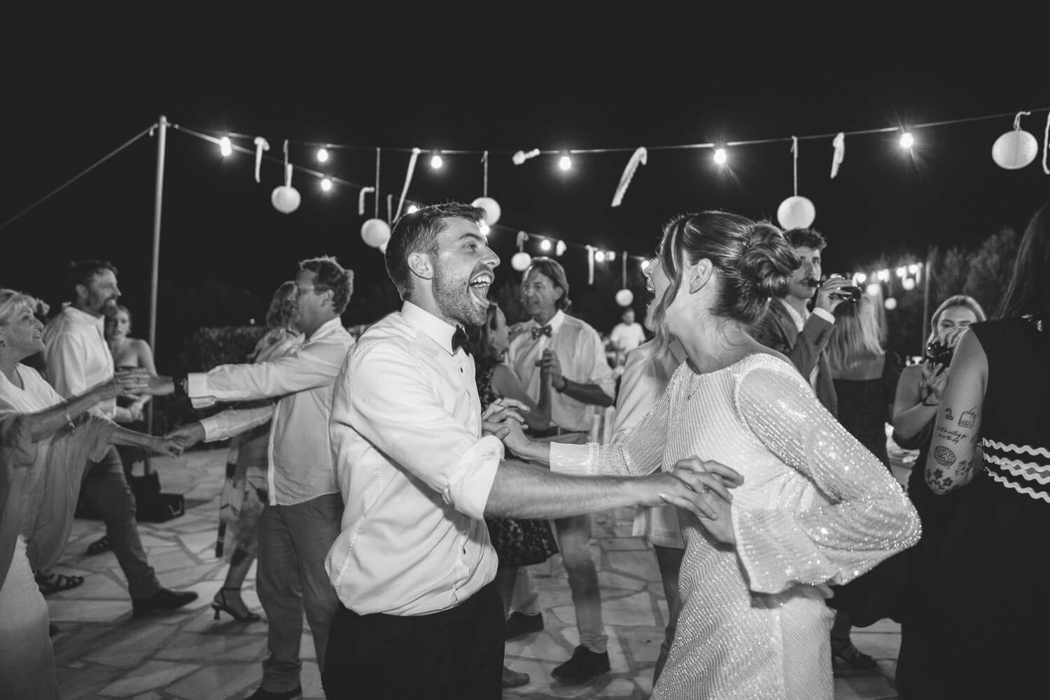 People dance together at a nighttime outdoor event with string lights illuminating the space.