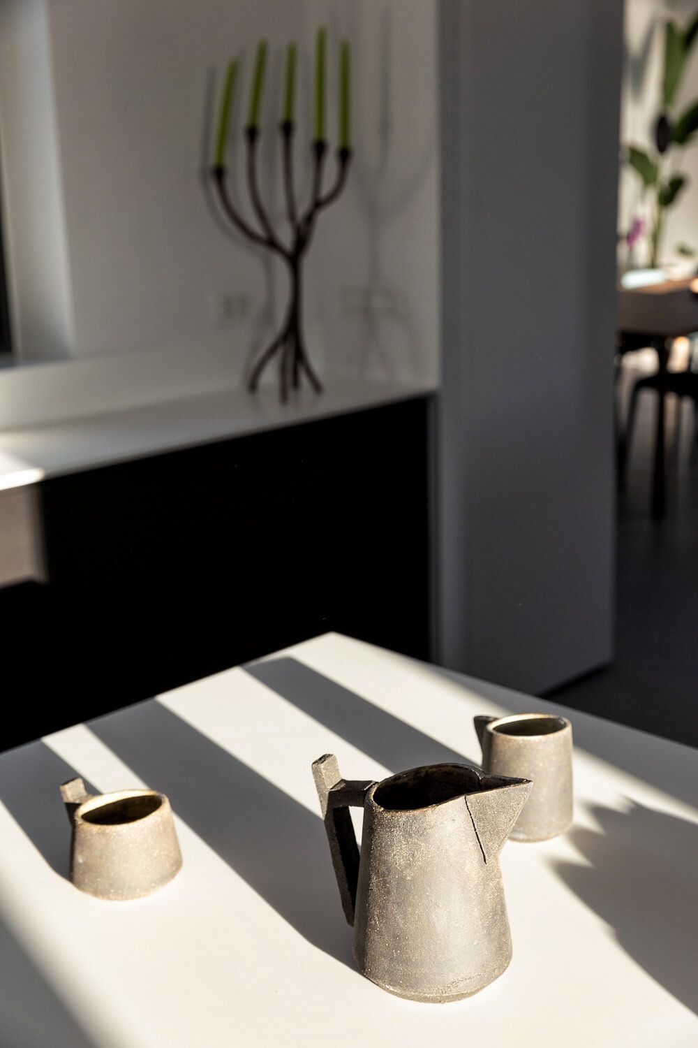 Ceramic pitchers and cup set on a white table with dramatic shadows.