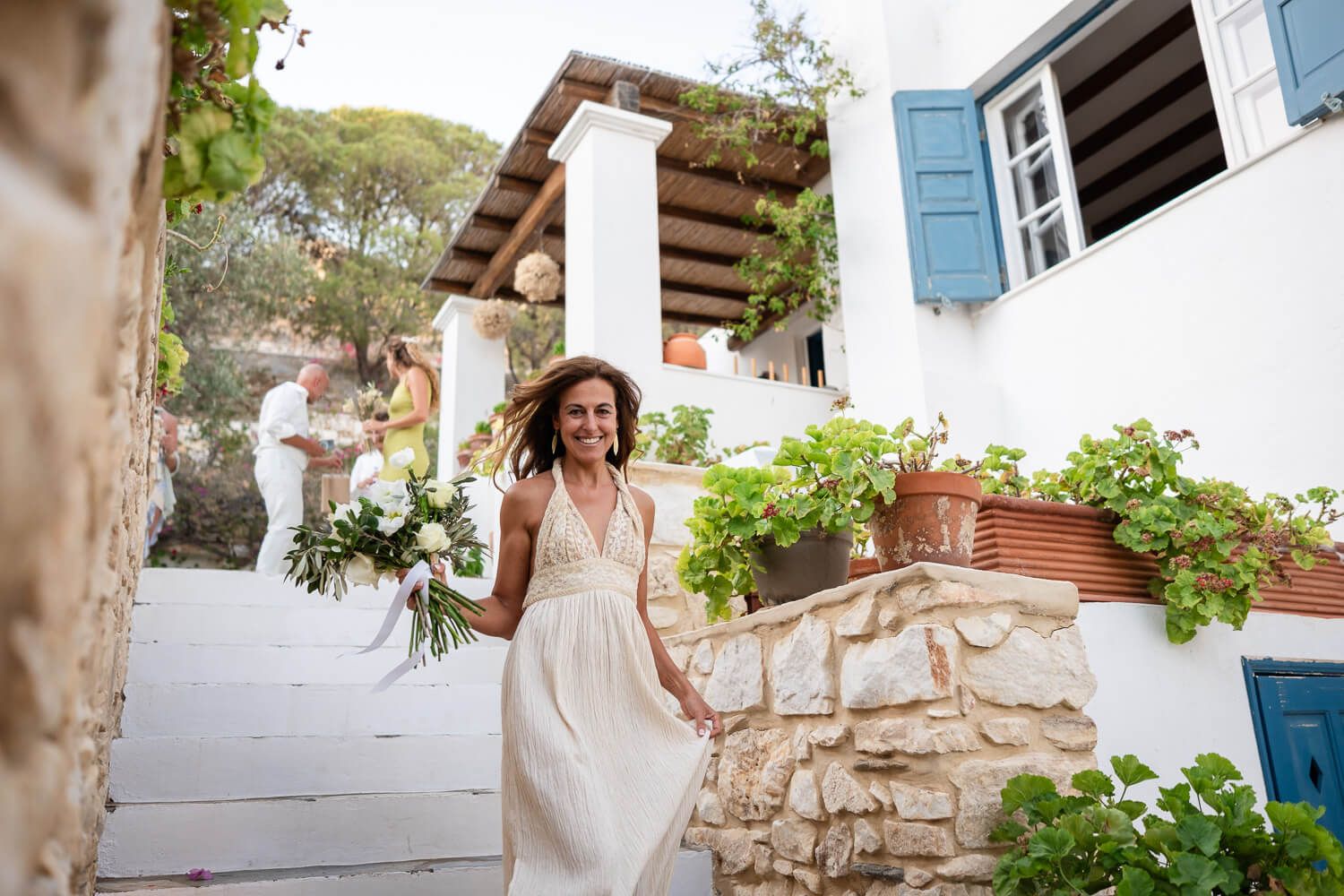 A joyful bride in a flowing white dress walks down steps to the reception area at Petra Farm Paros.