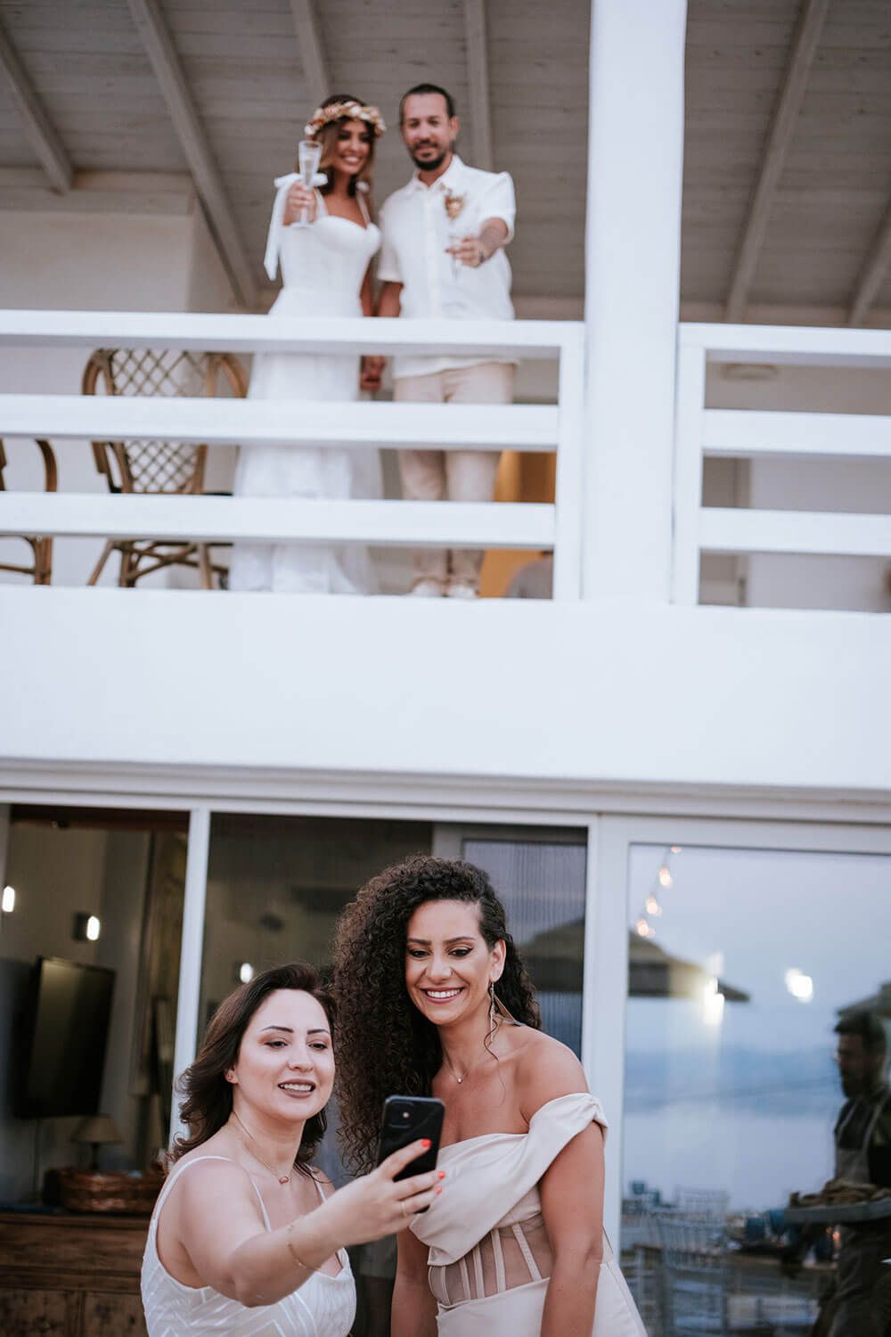 Wedding party members share a lighthearted moment while looking at a phone screen during an outdoor reception.