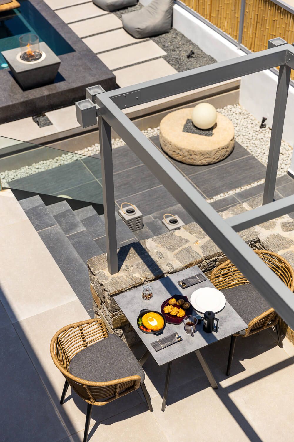 Modern outdoor patio furniture with gray metal frames and woven rattan seats arranged in a sunny setting.