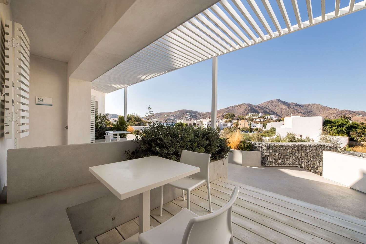 Modern white pergola with adjustable louvers creates a sleek outdoor living space against a mountain backdrop.