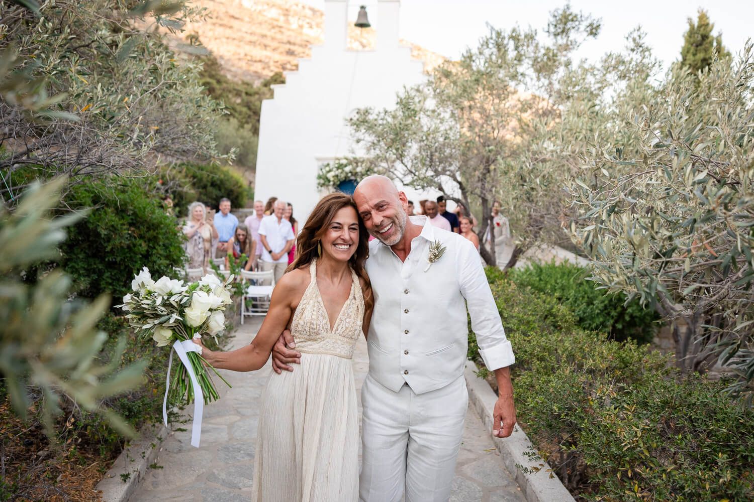 A romantic outdoor wedding ceremony with a lighthouse and flowering trees in the background.