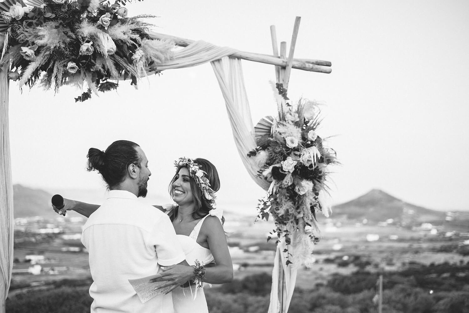 Black and white panoramic shot of an outdoor wedding ceremony with mountain views and floral arrangements.