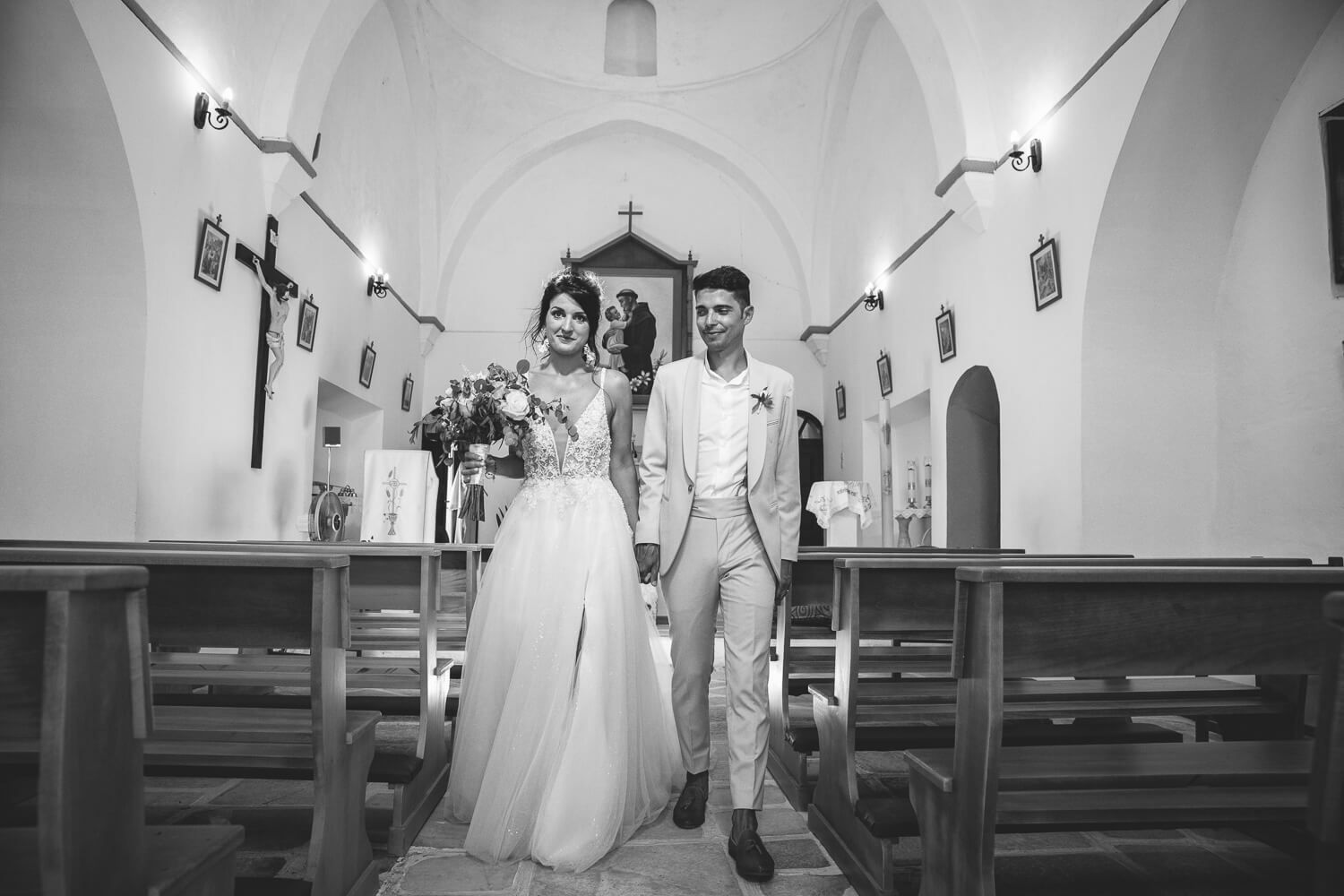 Happy Erika and Marco walking out of the church as guests throw rice and petals