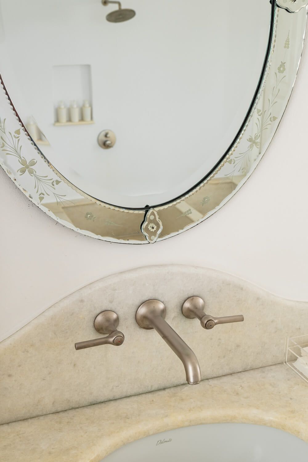 Modern brushed nickel wall-mounted faucet with oval mirror in a minimalist bathroom interior.