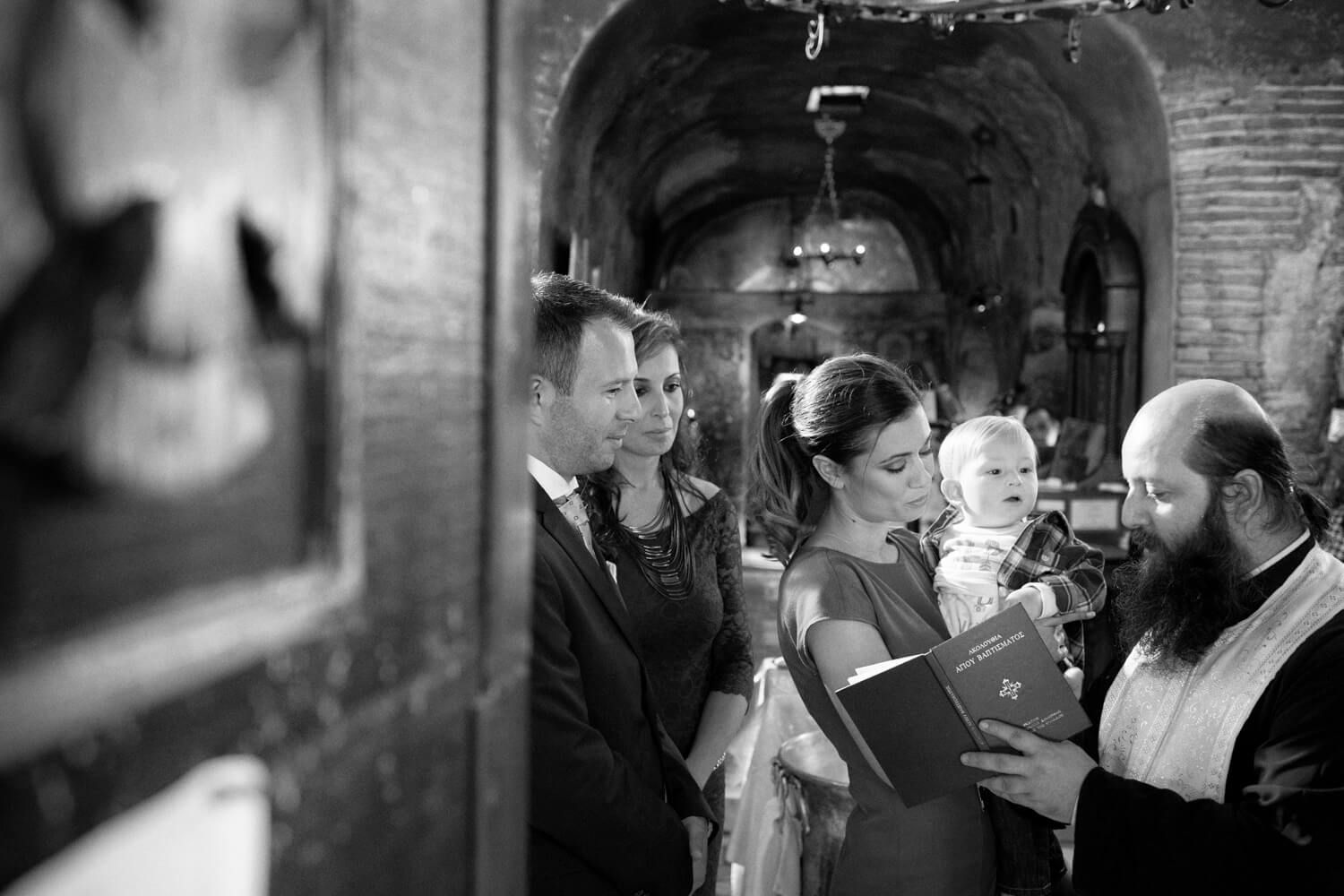 Black and white wedding ceremony photo with couple and priest in historic stone church setting.